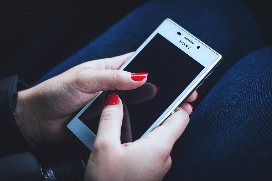 Woman with red nails holding white smartphone on blue jeans