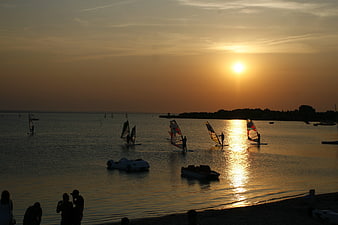 Windsurfers Silhouetted Against Golden Sunset on Calm Sea