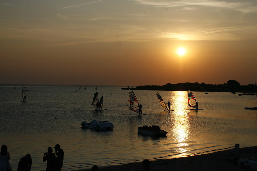 Windsurfers Silhouetted Against Golden Sunset on Calm Sea