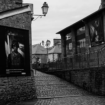 Black and white cobblestone street in Bayeux with museum posters