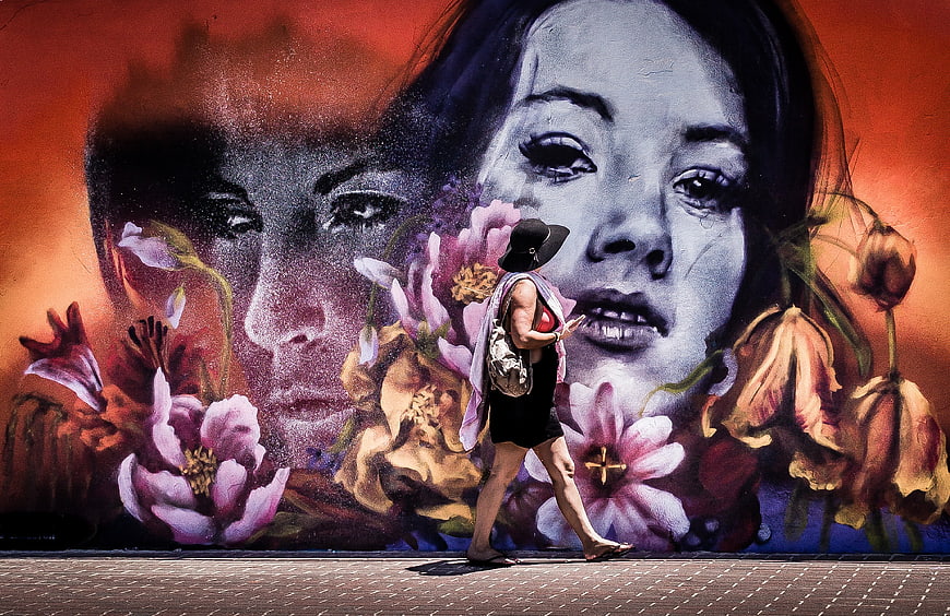 Woman walking past large colorful street art mural with flowers
