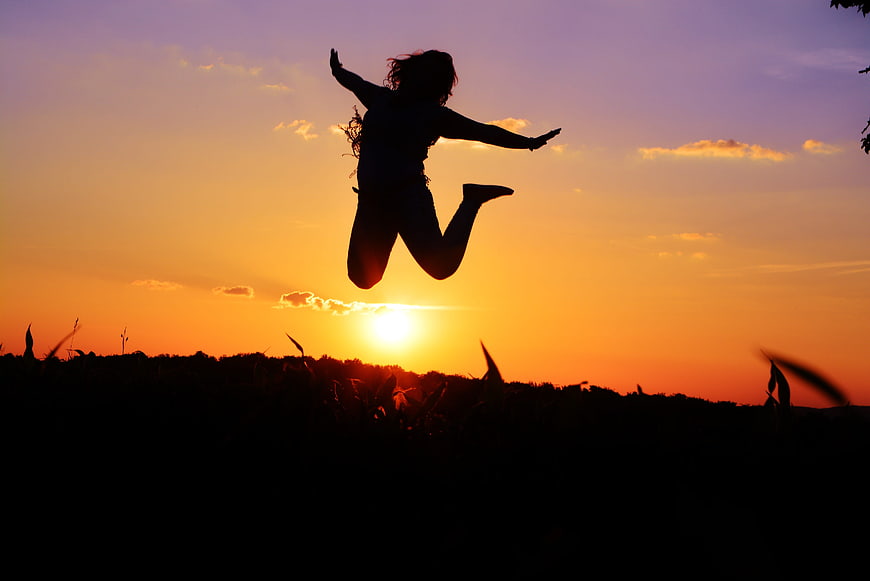 Silhouette of Woman Jumping in Field at Sunset