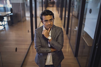 Thoughtful businessman in grey suit standing in modern office hallway