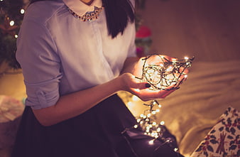 Woman holding glowing Christmas lights in cozy bedroom