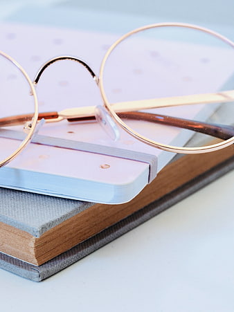 Minimalist stack of notebooks with gold-rimmed glasses and pen