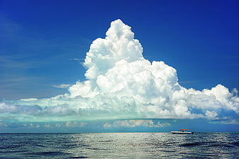 Massive cumulonimbus cloud over ocean with small boat