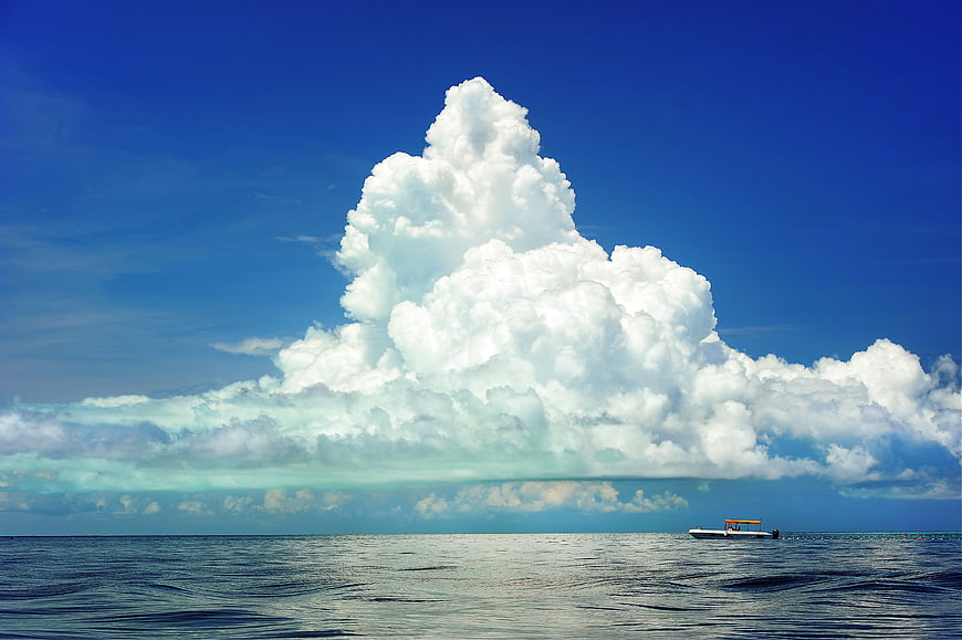 Massive cumulonimbus cloud over ocean with small boat