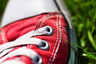 Close-up of red sneaker laces and eyelets on green grass