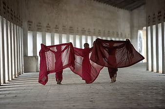 Young Buddhist Monks Running with Red Fabric in Corridor