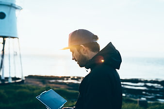 Man with Tablet Near Lighthouse at Sunset