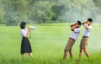 Asian students shouting with megaphone in green field