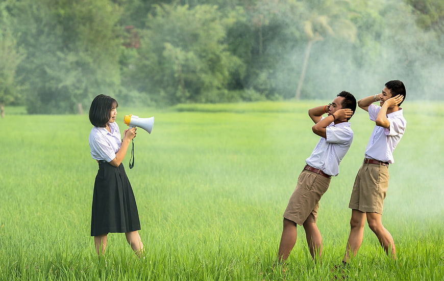 Asian students shouting with megaphone in green field