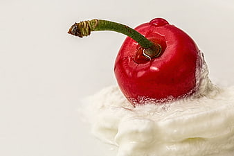 Close-up of a fresh red cherry on a swirl of white whipped cream