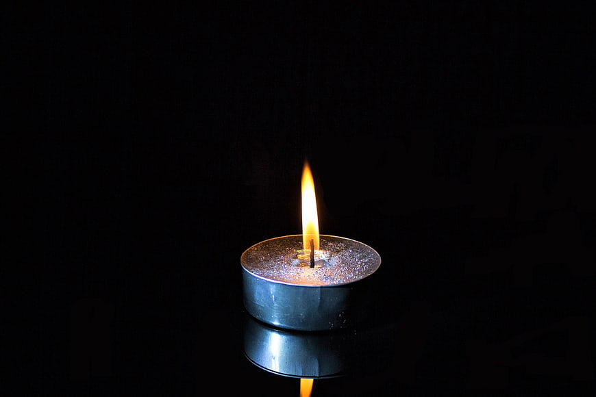 Single lit tealight candle on black reflective surface