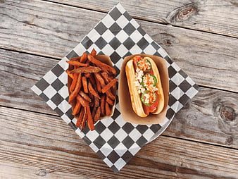 Top view of hot dog and sweet potato fries on checkered paper