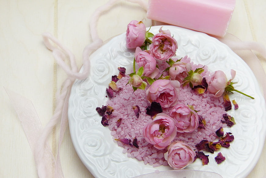 Pink bath salts with fresh roses and soap on white plate