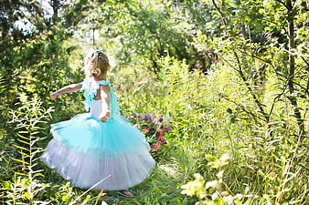 Little girl in blue tutu dress running through sunny forest