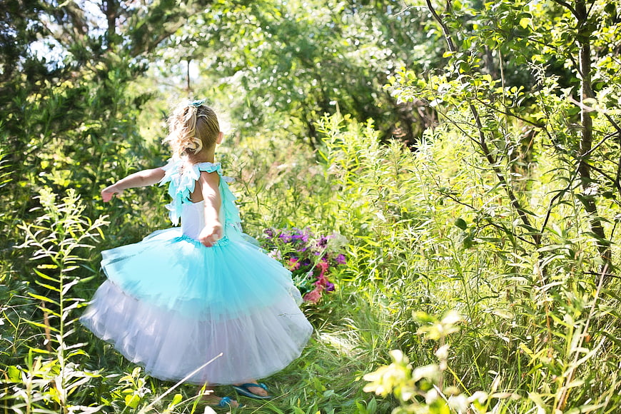 Little girl in blue tutu dress running through sunny forest