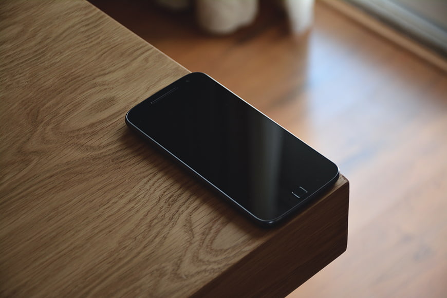 Black smartphone resting on wooden table edge
