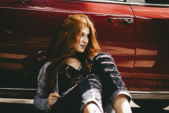 Redhead woman sitting by vintage red car