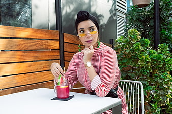 Stylish woman in striped dress drinking juice at cafe