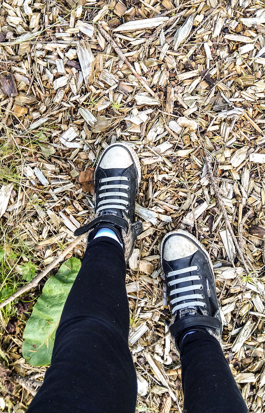 First-person view of black sneakers on wood chips