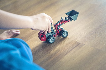 Child Playing With Red Toy Wheel Loader On Wooden Floor