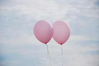 Two Pink Balloons Floating Against a Cloudy Blue Sky
