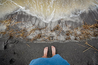 Bare feet on black volcanic sand beach with ocean waves