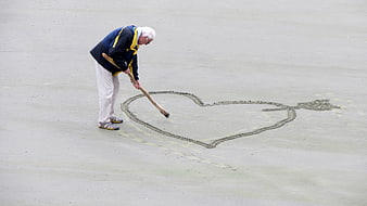 Senior man drawing heart in wet sand on beach