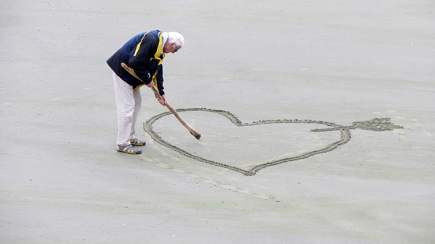 Senior man drawing heart in wet sand on beach