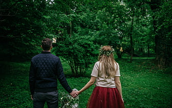 Couple holding hands walking away in green forest