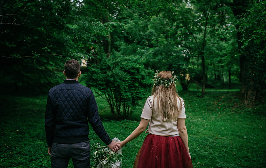 Couple holding hands walking away in green forest
