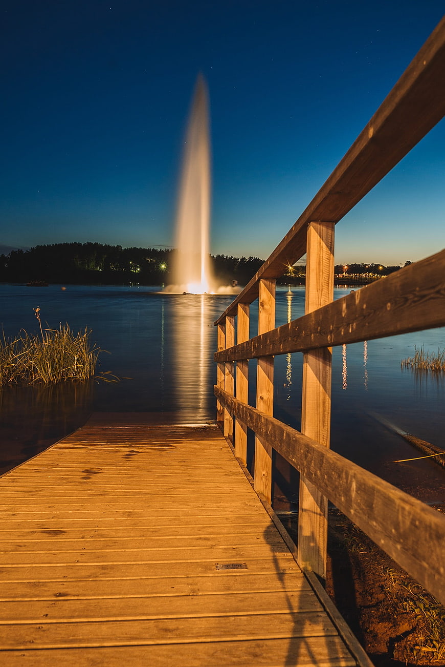 Wooden pier leading to illuminated fountain at night