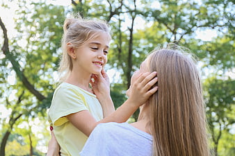 Mother holding smiling daughter in sunny park