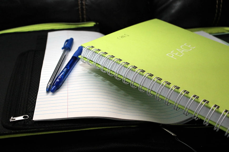 Green Spiral Notebook with Blue Pens on Black Bag