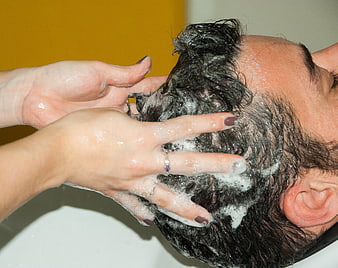 Close-up of hairdresser washing client's hair with shampoo foam