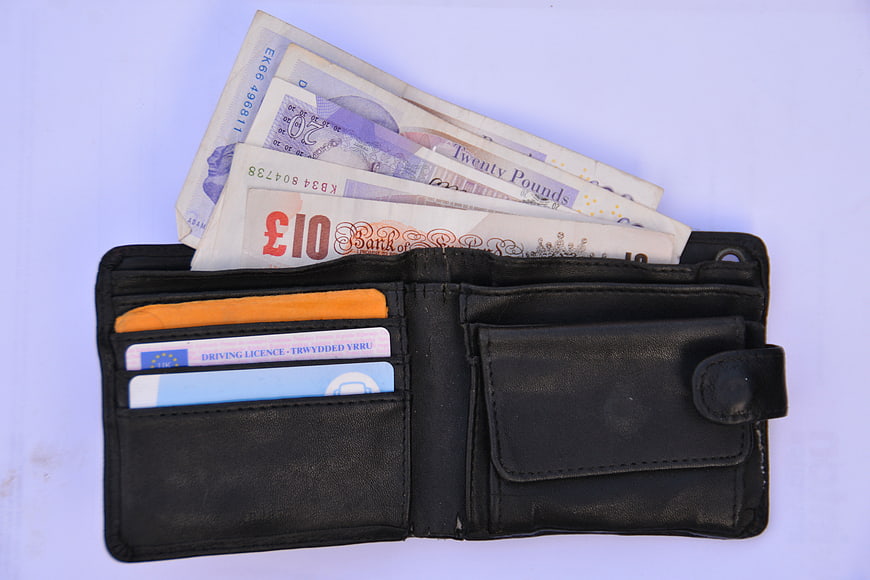 Open black leather wallet with British banknotes and cards on white background