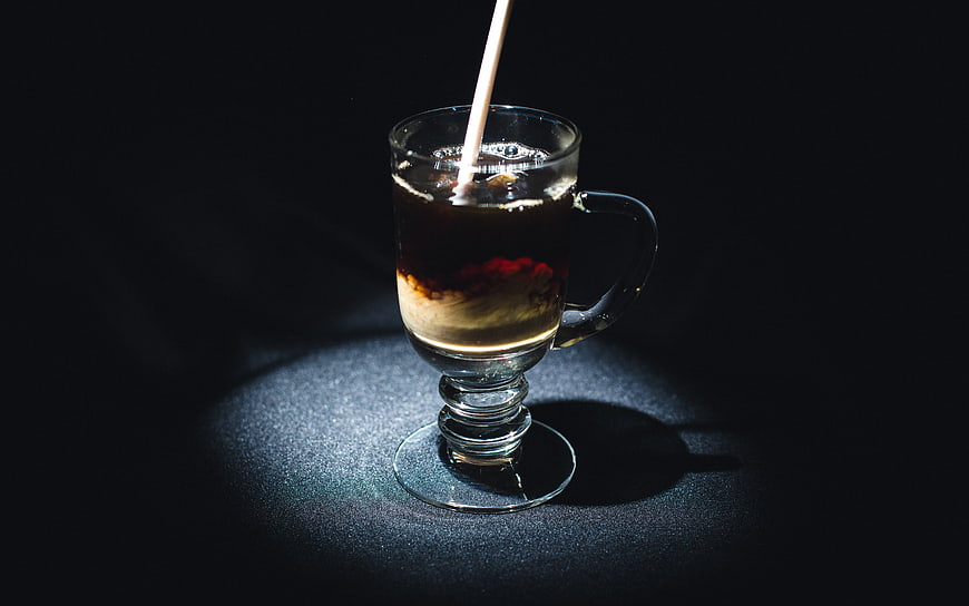 Dark moody iced coffee with cream swirl in glass mug