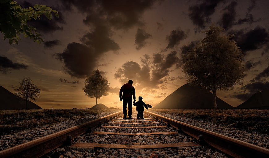 Silhouette of Father and Son Walking on Railroad Tracks at Sunset