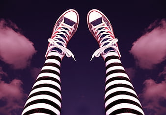 Legs in striped tights and red sneakers against a purple sky