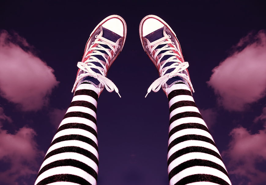 Legs in striped tights and red sneakers against a purple sky