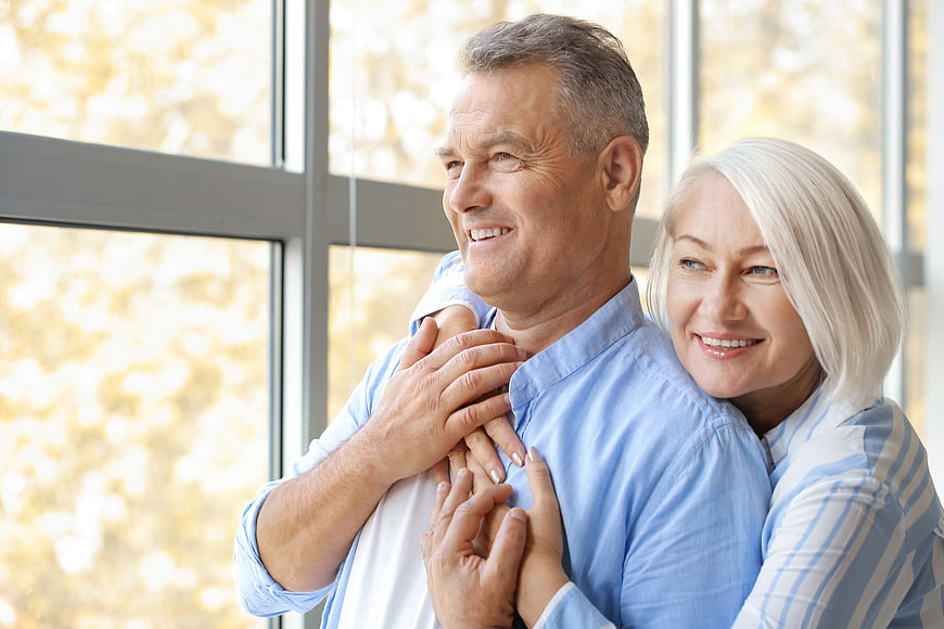 Happy Senior Couple Embracing Indoors by Window