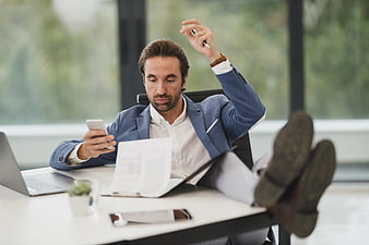 Stressed businessman with feet on desk checking phone