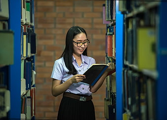 Asian female student reading book in library aisle