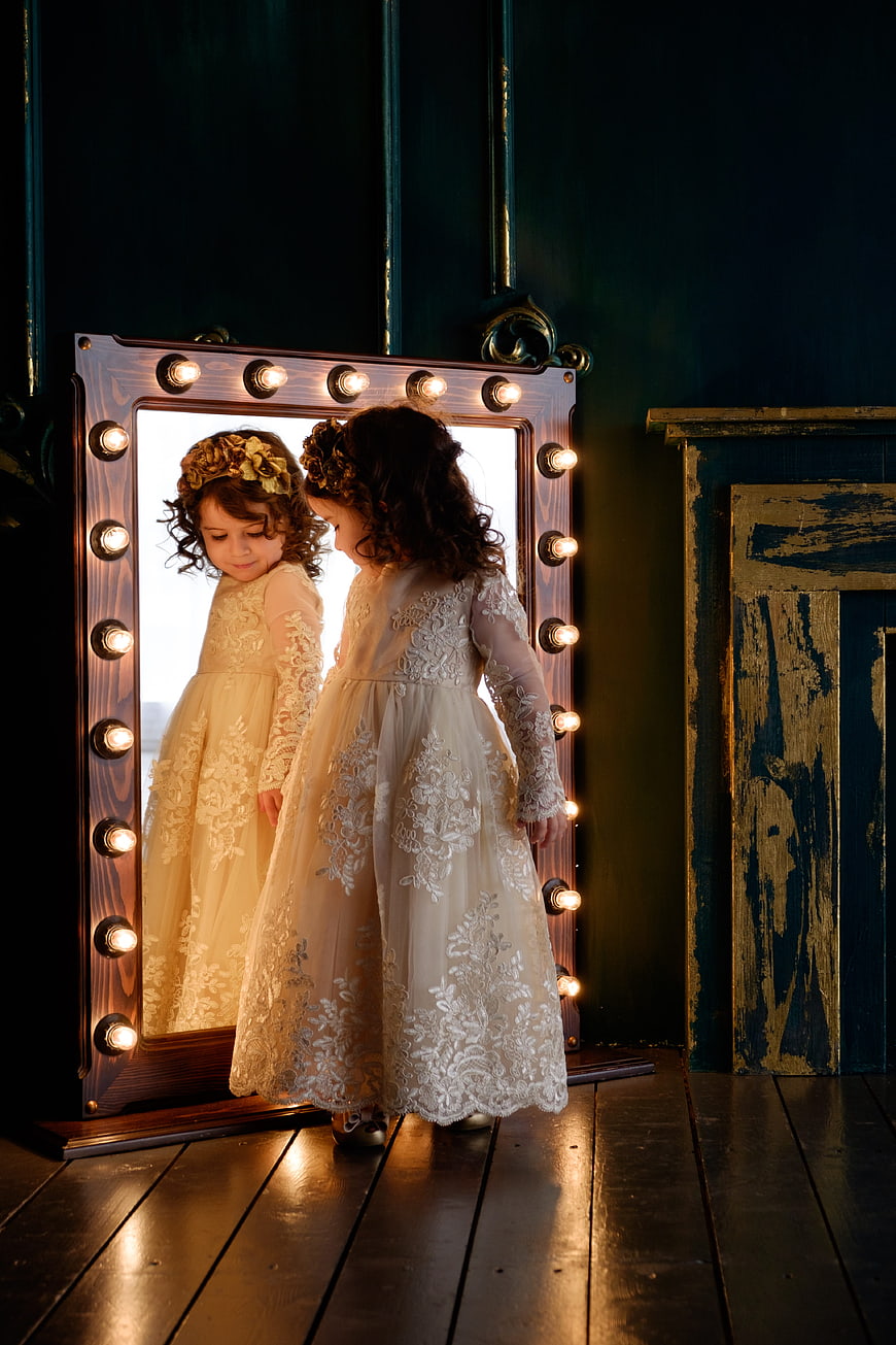 Little girl in lace dress looking into vintage vanity mirror