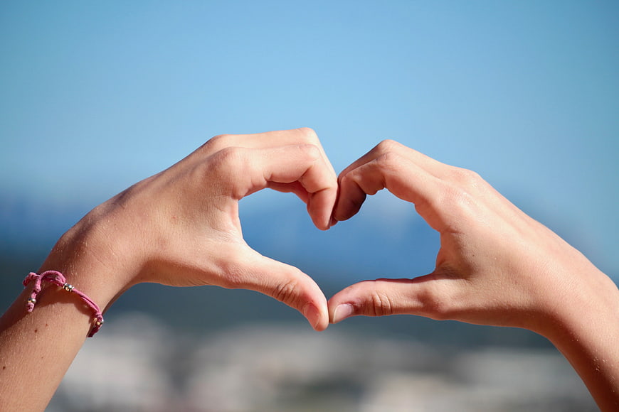 Hands forming heart shape against blue sky background