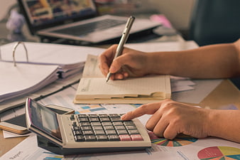 Close-up of hands using calculator and writing on financial reports