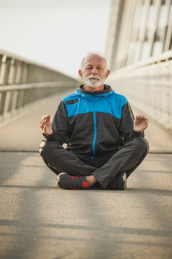 Senior man meditating outdoors on a bridge in athletic wear