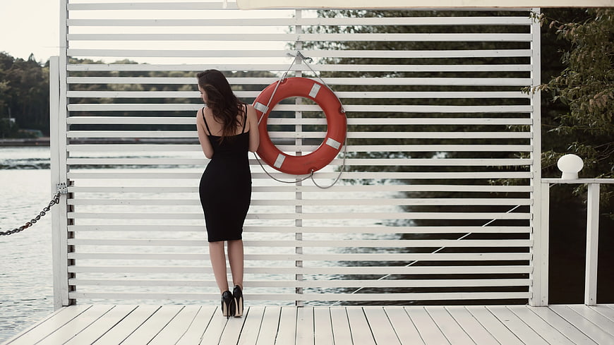 Woman in Black Dress Standing by Red Lifebuoy on White Dock